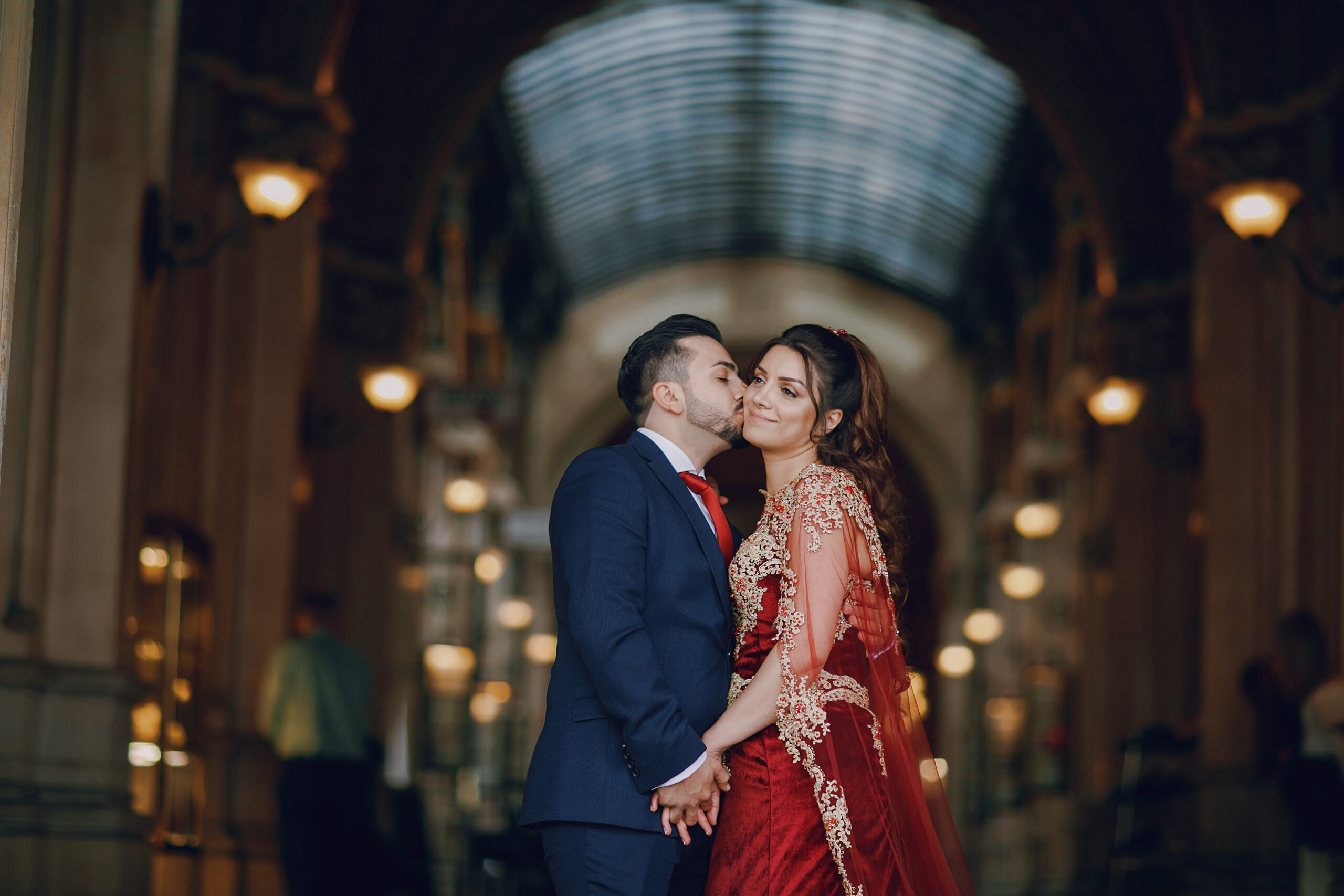 Beautiful woman in a long red dress walks around the city with her husband in a blue suit and with a beard